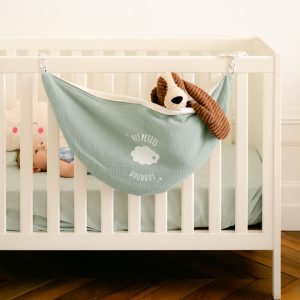 Un doudou est rangé dans un hamac accroché au lit d'un bébé.